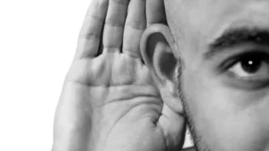 Close-up of a man with his hand cupped around his ear to hear better.