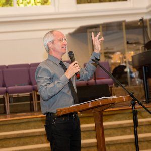 A racial reconciliation advocate speaking into a microphone and gesturing at a church-hosted event.