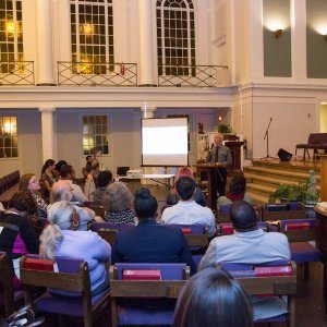 A man speaking at the podium of a church about racial reconcilation to a crowd of attendees.