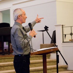 A man speaking into a microphone and pointing emphatically during a speech about racial reconciliation.