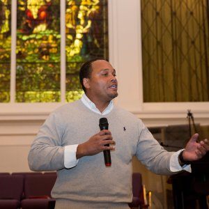 A man speaking and gesturing passionately during a racial reconciliation speech at a church-hosted event.