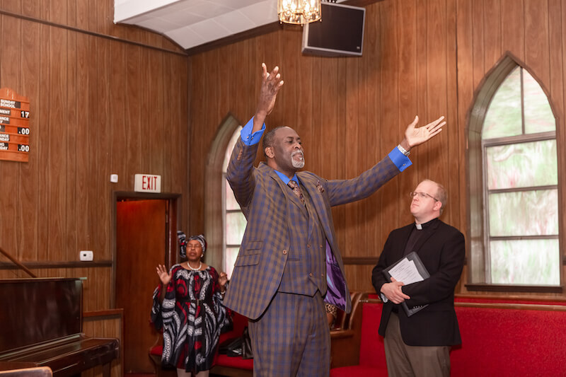 A man and woman raising their hands to greet people sitting in the church.