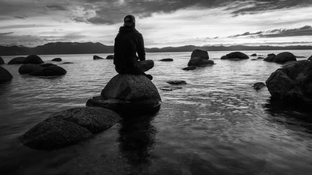 Man sitting cross-legged on rocks jutting out of the ocean.