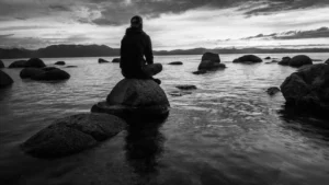 Man sitting cross-legged on rocks jutting out of the ocean.